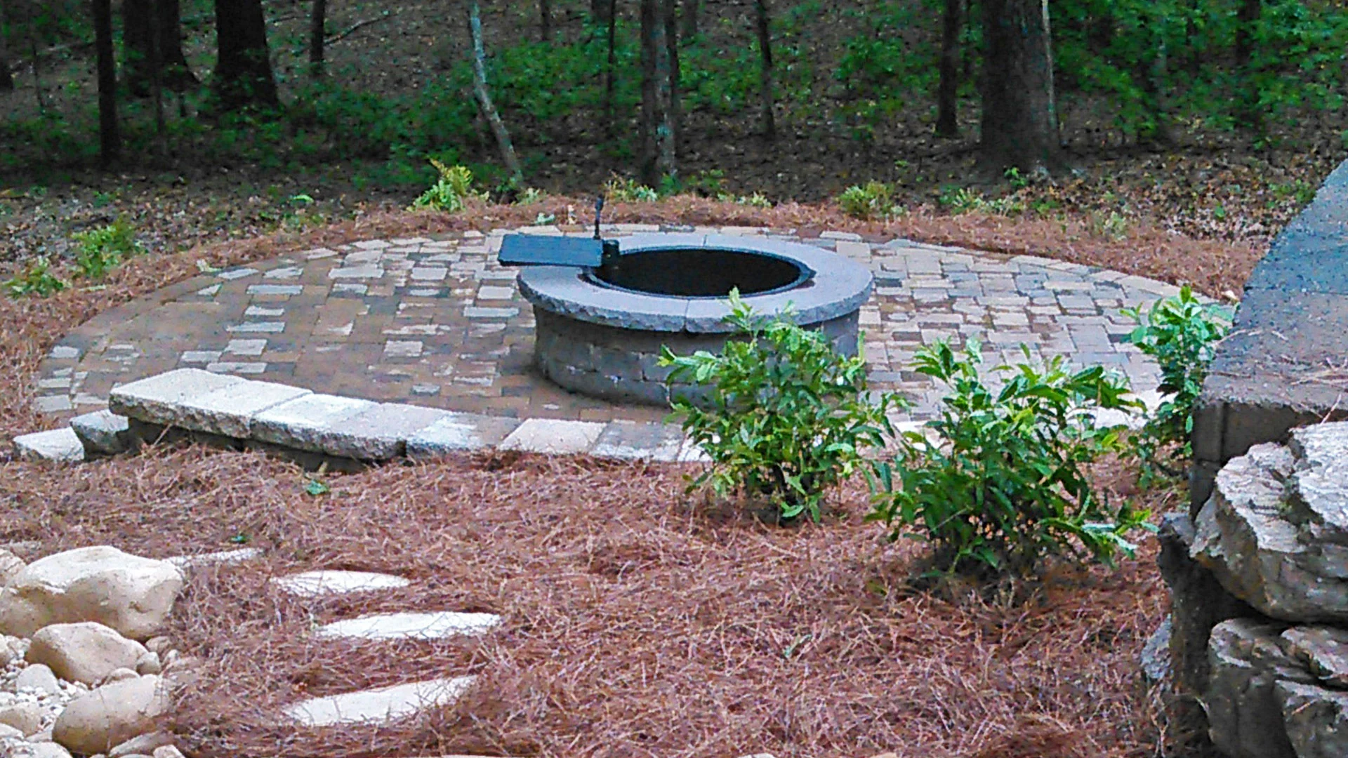 A round fire pit with a paver patio, seating wall, and retaining wall.