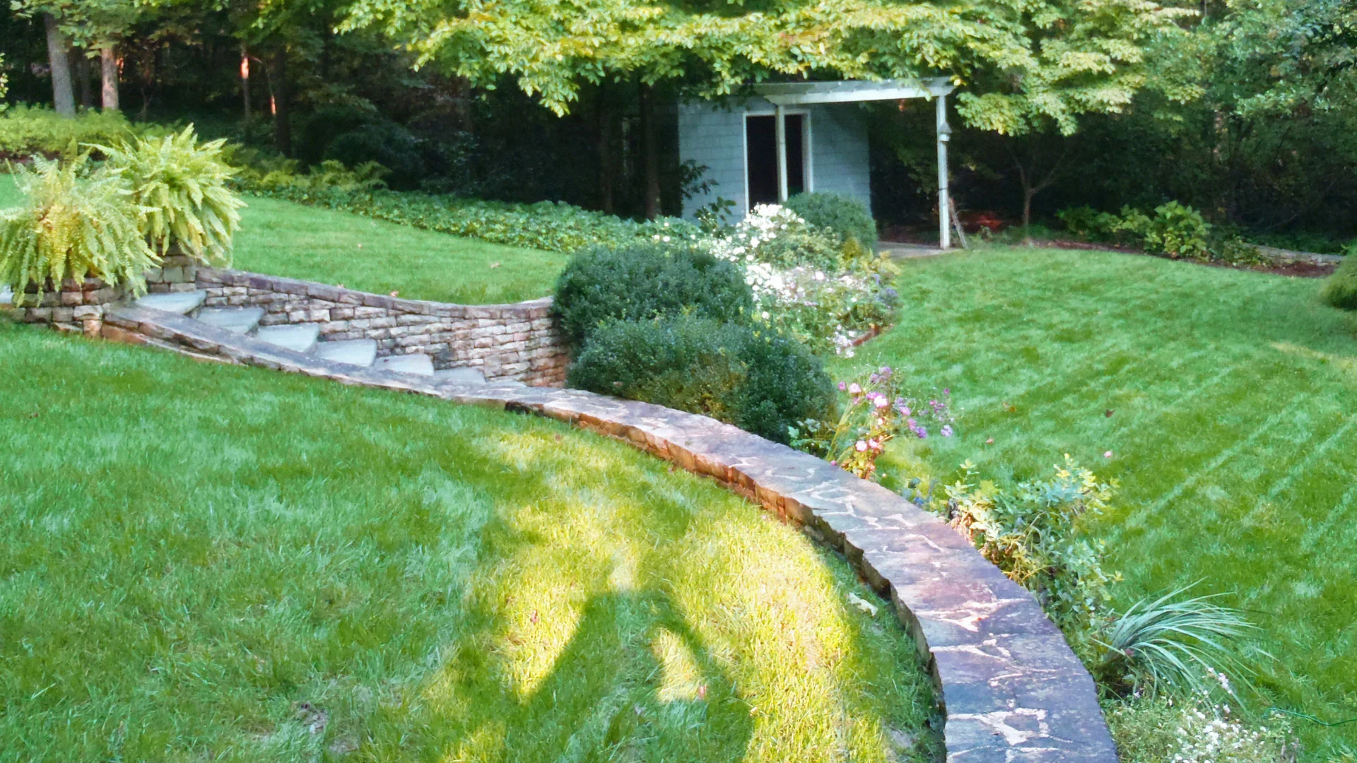 Backyard with hardscaping, steps, retaining wall, and mowed lawn.